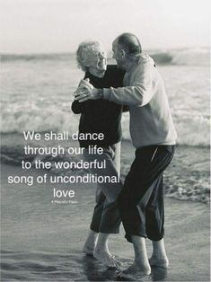 an older couple embracing each other while standing on the beach with their arms around each other