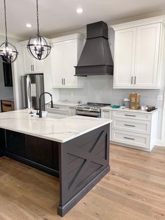 a large kitchen with white cabinets and black island in the center is surrounded by wood flooring