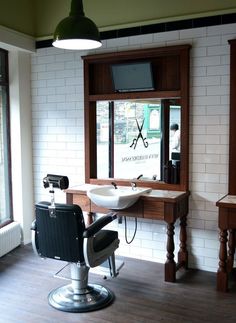 a barber chair in front of a sink and window with a tv on the wall