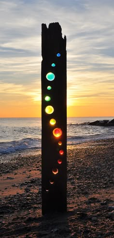 a piece of wood sitting on top of a sandy beach next to the ocean at sunset