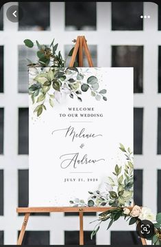 a welcome sign with greenery on it and an easel for the guests to use