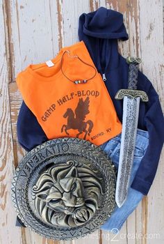 an orange hoodie, blue sweatshirt and two swords are laid out on a wooden surface