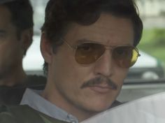 a man wearing sunglasses and a mustache sitting in a car with another man behind him