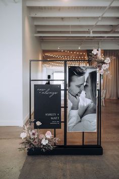 a couple kissing in front of a sign with flowers on the floor and lights behind it