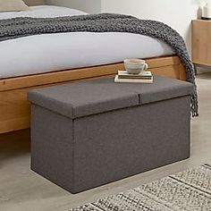 a gray ottoman with a cup on it in front of a bed and rugs