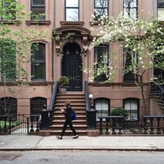 a person walking down the sidewalk in front of a building with stairs and trees on both sides