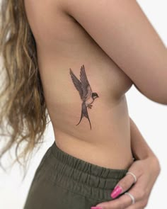 a woman's stomach with a small bird tattoo on her left side ribcage