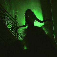 a woman with long hair is walking down the stairs in a dark room, holding her arms out