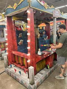 a man standing in front of a red and blue carnival booth with lights on it