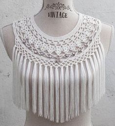 a mannequin wearing a white crochet and tasseled neck piece