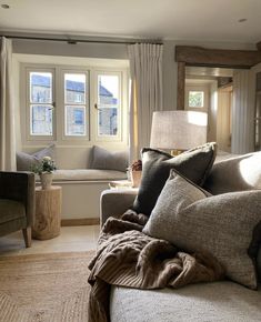 a living room filled with lots of furniture next to a window covered in blankets and pillows