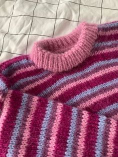 a pink and blue sweater laying on top of a bed next to a white sheet