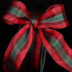 a red and green ribbon tied on top of a black box with a bow around it