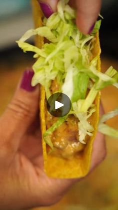 a person holding up a taco with lettuce and meat in the middle