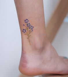 a small flower tattoo on the ankle is shown in blue and green colors, with tiny flowers