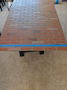 a dog is standing next to a table made out of bricks and blue tape on the floor