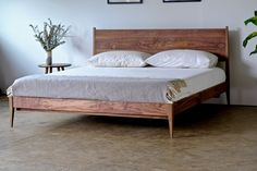 a wooden bed with white sheets and pillows in a room next to a potted plant