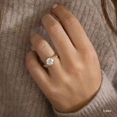 a woman's hand wearing a gold ring with a round diamond in the middle