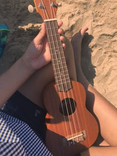 a person sitting on the beach with a ukulele in their hand and sand behind them