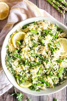 a white bowl filled with pasta and asparagus on top of a wooden table