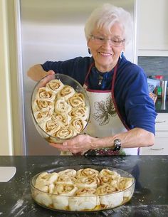 an older woman holding a pan full of cinnamon rolls