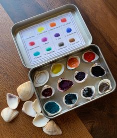 an open tin filled with lots of different colored paints on top of a wooden table