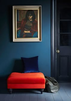 an orange bench in front of a blue wall with a painting on the wall above it