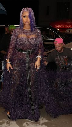 a woman with purple hair standing next to a man in a pink hat and black dress