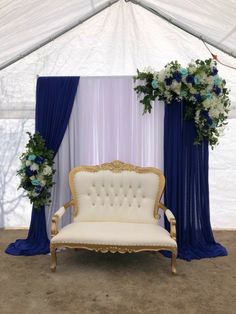 a white couch sitting in front of a blue and white drape covered wall with flowers on it