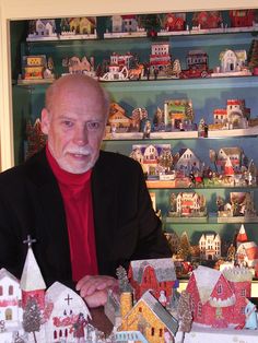 an older man sitting at a table in front of a display of christmas village houses