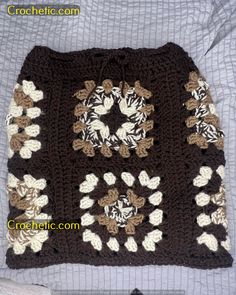 a crocheted square with flowers and leaves on the side, sitting on top of a bed