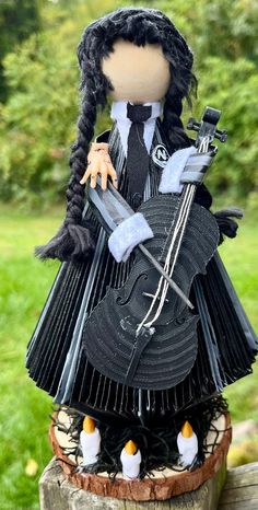 a doll is sitting on top of a tree stump with a violin in her hand