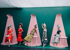 five women sitting on stools in front of a green wall with pink and blue walls