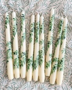 six candles with green leaves on them are lined up in a row against a patterned background