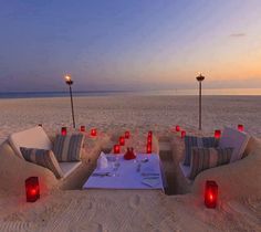 an outdoor seating area is set up on the beach with candles and wine bottles in the sand