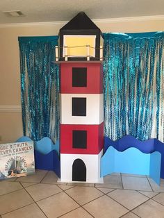 a lighthouse made out of cardboard sitting on top of a tile floor next to a blue curtain