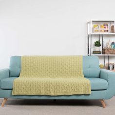 a blue couch with a green blanket on it in a room next to a book shelf