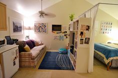 a living room with a bed, couch and bookshelf next to a kitchen