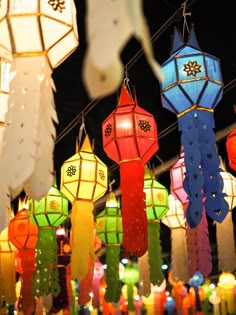 many colorful lanterns hanging from strings in a room with lights on the ceiling and candles lit up behind them