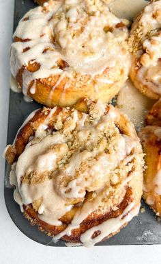 cinnamon rolls covered in icing on top of a baking sheet with crumbs