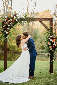 a bride and groom kissing under an arch decorated with flowers at their outdoor wedding ceremony