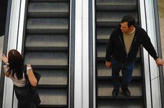 two people walking down an escalator with their arms in the air and one person standing at the bottom