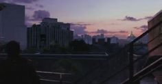 a man standing on top of a balcony next to a cityscape at sunset