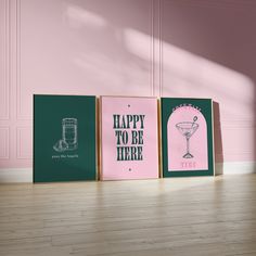 three framed posters on the floor in front of a wall with pink walls and wooden floors