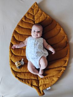 a baby laying on top of a yellow leaf shaped pillow with hair clips in it's mouth