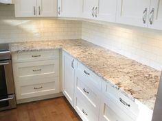 a kitchen with white cabinets and marble counter tops