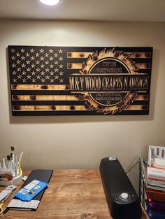 a wooden table topped with a laptop computer next to an american flag on the wall