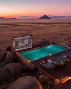 an outdoor swimming pool surrounded by rocks and boulders at dusk with the sun setting in the distance