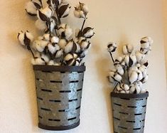 two metal buckets holding cotton plants against a white wall, one is made out of tin cans