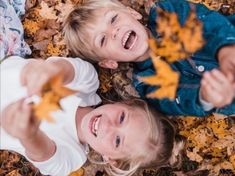 two young children are playing with leaves on the ground in the fall season, looking up at the camera